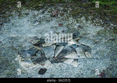 Broken ice fragments scatter over frosted grass, revealing a frozen pool disrupted on a cold winter day Stock Photo