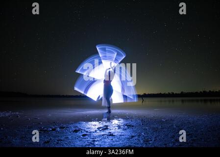 person standing in the dark posing in front of light on a lake Stock Photo