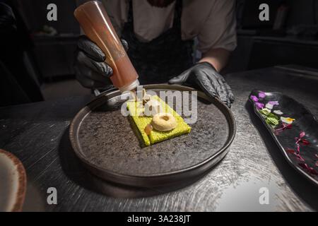 Chef adding sauce to modern gourmet dish in restaurant kitchen Stock Photo