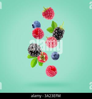 falling raspberries, blackberries and blueberries on a light green background. Stock Photo
