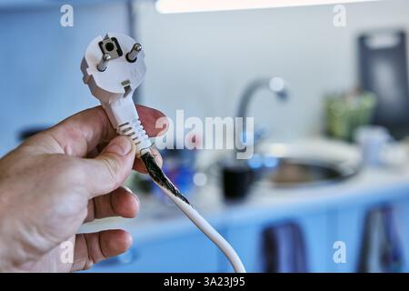 Burnt out cable with an electrical plug in hand of user who has overloaded an extension cord with tee. Stock Photo