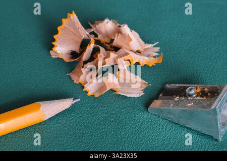 Yellow pencil and sharpener with shavings on green background Stock Photo