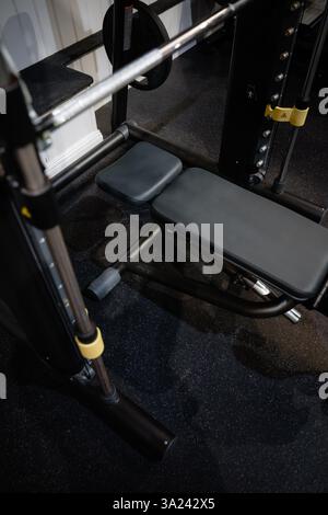A black bench with a yellow and black handle bar. The bench is in a gym Stock Photo