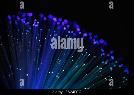 Glowing fiber optic cables with vibrant blue and purple bokeh lights on a dark background, representing fast internet, data transfer, and technology Stock Photo