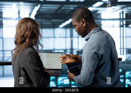 Programmers in data center facility workplace use laptop to calibrate supercomputers energy usage. Server room IT staff members code on notebook, doing maintenance on equipment rigs Stock Photo