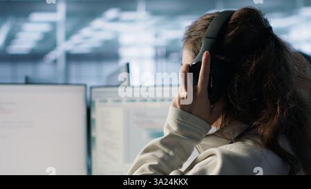 Engineer typing on computer in server hub, checking recovery plan, monitoring data center energy consumption, listening music. Technician wearing headphones inspecting rackmounts, camera A close up Stock Photo