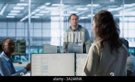 Manager overseeing server room holding impromptu meeting with employees. Supervisor in server hub, asking for attention to offer feedback to workers after doing inspection, camera A Stock Photo