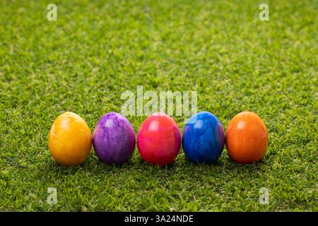 Five multi-colored Easter eggs stand in a row on the lawn Stock Photo