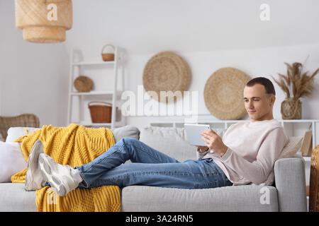 Young man using tablet computer on sofa at home Stock Photo