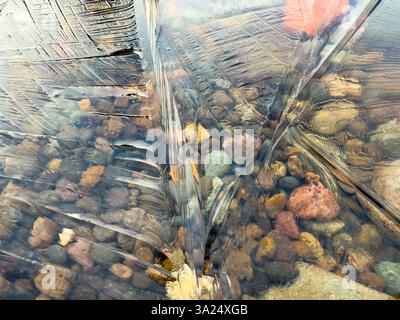 Pattern in ice of frozen water above layer of pebbles in multiple colors Stock Photo