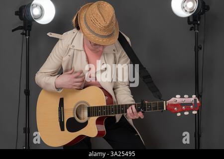 Inspiration female guitarist playing six string classical guitar, looking down at strings on instrument. Playful woman musician standing full length o Stock Photo