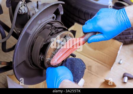 Hands equipped with gloves clean brake components in workshop setting while performing maintenance tasks car Stock Photo