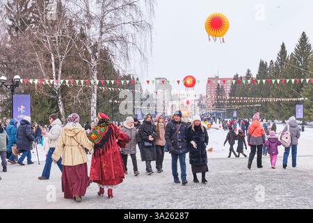 Yekaterinburg, Russia - February 26, 2025: People enjoying Maslenitsa celebration in city park. Park decorated with colorful banners and sun-shaped or Stock Photo