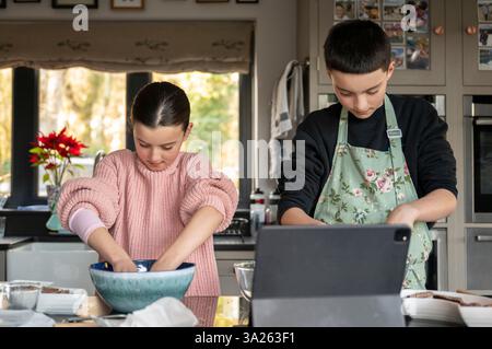Boy and girl baking together in kitchen using tablet. Stock Photo