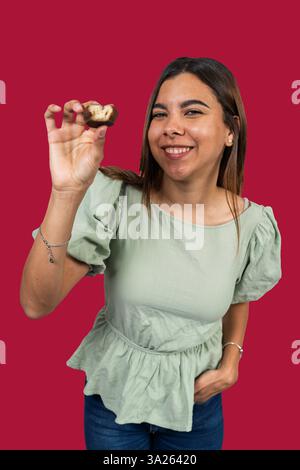Happy latin woman holding a bite of chocolate cake on red background Stock Photo