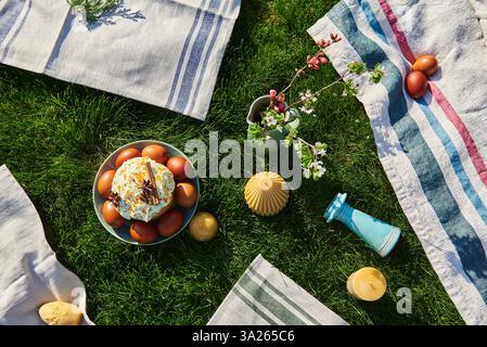 Festive outdoor Easter picnic setup with a traditional Easter cake and brown dyed eggs on a green lawn. Linen textiles, candles, and flowers Stock Photo