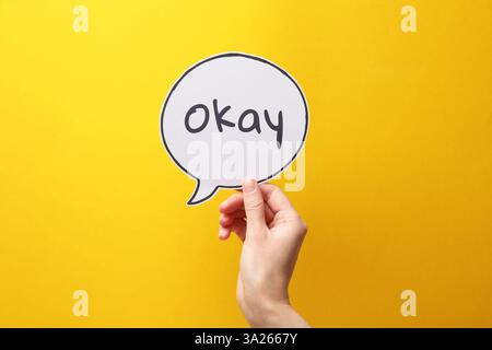 Woman holding paper speech bubble with word Okay on yellow background, closeup Stock Photo