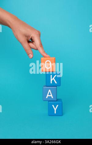 Woman making word Okay with colorful cubes on light blue background, closeup Stock Photo