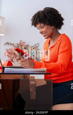 African American student using smartphone while studying at home with laptop.Vertical Stock Photo
