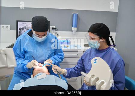 Two dentists working together, performing a dental procedure on a patient lying in a dental chair, using specialized equipment Stock Photo
