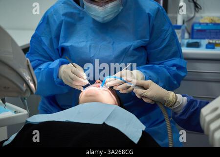 Dentist and assistant performing dental procedures on a patients teeth in a modern clinic, ensuring optimal oral health and hygiene Stock Photo