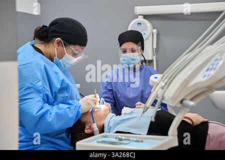 Two dentists performing a check up on a patient lying in a dentist chair, wearing protective equipment Stock Photo