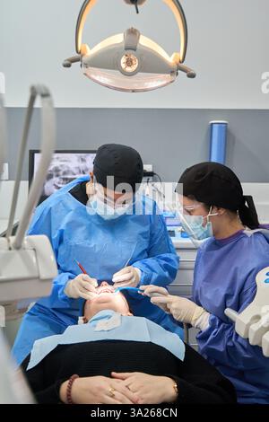 Two dentists working together performing a dental procedure on a patient lying on a dentist chair Stock Photo