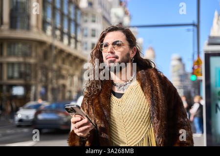 Latin transgender walking down a city street using a smartphone, wearing elegant clothes and long hair Stock Photo