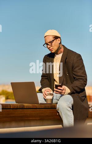 Handsome man in a chic outfit focuses on his laptop while sipping coffee in a sunny location. Stock Photo