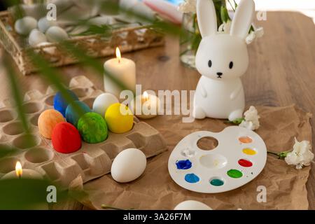 A lively display of decorated Easter eggs arranged around a white bunny figurine. The palette, filled with vibrant paints, is ready for creativity, wh Stock Photo
