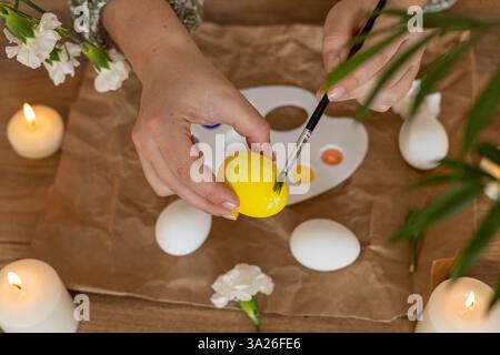 Hands carefully paint white eggs using a palette of vibrant colors surrounded by candles and flowers. This activity captures the festive spirit of Eas Stock Photo