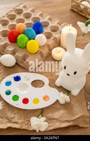 A lively display of decorated Easter eggs arranged around a white bunny figurine. The palette, filled with vibrant paints, is ready for creativity, wh Stock Photo