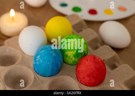 Brightly colored Easter eggs are arranged on a table alongside a paint palette and lit candles. This festive setup captures the joyful spirit of sprin Stock Photo
