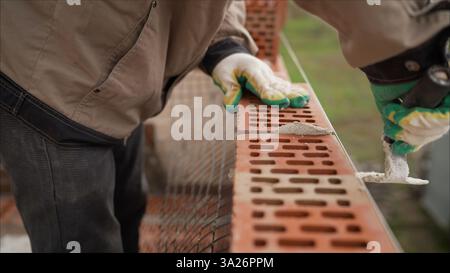 Worker in Close up of industrial bricklayer installing bricks and mortar cement brick on construction site. Worker builds a wall of colored brick. Stock Photo