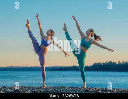 Two women in athletic wear practicing high kicks on a beach at sunset. Bainbridge Island, WA, USA Stock Photo