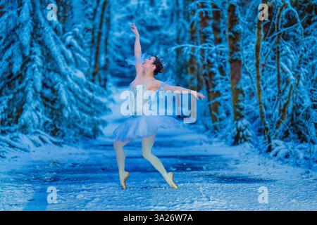 Ballet dancer in a snow-covered forest wearing a white tutu and performing a graceful pose. WA, USA Stock Photo