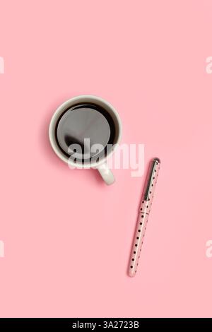 A pen and a cup of coffee on a pink background in a top view Stock Photo