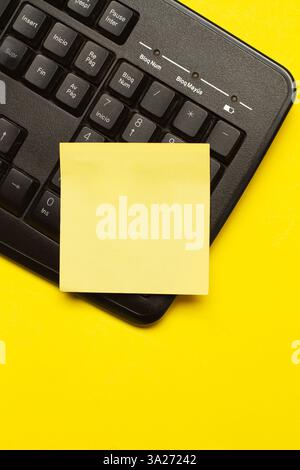 A blank yellow paper note on a black computer keyboard on a yellow background Stock Photo