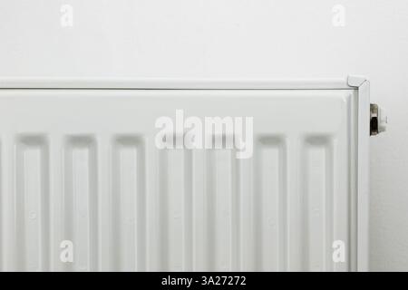 Close-up of a white metal radiator with a temperature control valve. Modern home heating system, energy efficiency concept. Minimalistic interior with Stock Photo