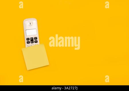 A blank yellow sticky paper over a telephone handset on a yellow background with copy space Stock Photo