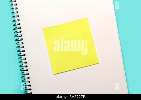 A blank yellow sticky paper on a blank page of a notepad on a light blue background Stock Photo
