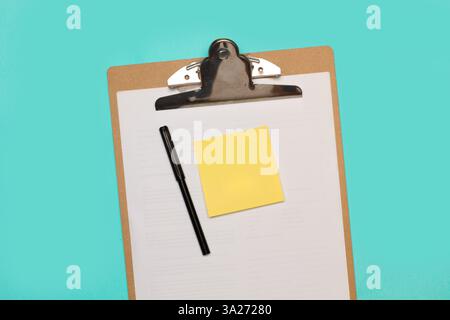 A blank yellow sticky paper and a black marker on a clipboard with white paper sheets on a light blue background Stock Photo
