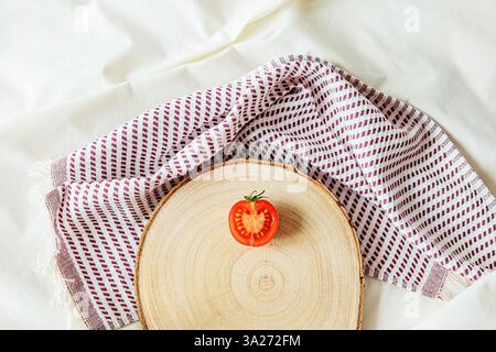 A single sliced cherry tomato placed on a rustic wooden board with a linen napkin. Minimalist food composition with natural light, organic textures, a Stock Photo