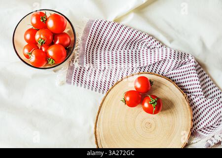 Fresh cherry tomatoes on a rustic wooden board with a linen napkin. A glass bowl filled with tomatoes in the background. Natural light and organic tex Stock Photo