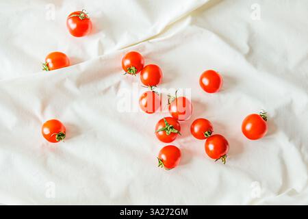 Cherry tomatoes scattered on white fabric. Natural light highlights their vibrant color and texture, creating a fresh, minimalist food composition per Stock Photo