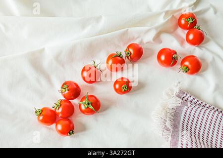 Cherry tomatoes scattered on a white fabric with a linen napkin. Natural light enhances their vibrant color and texture, creating a fresh, organic foo Stock Photo