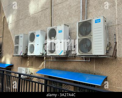 A collection of air conditioning units attached to a building's facade, showing fans and a blue shade. Stock Photo