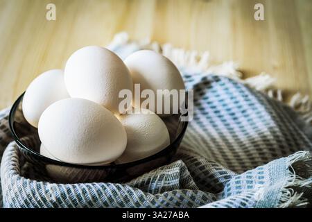 A close-up of fresh white eggs in a glass bowl on a rustic kitchen towel. Soft natural light highlights the texture, creating a cozy feel. Ideal for f Stock Photo
