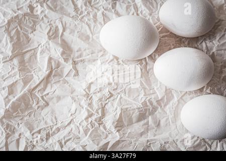 White eggs placed on crumpled paper, creating a minimalist and organic composition. Soft natural light enhances textures, making it ideal for Easter, Stock Photo