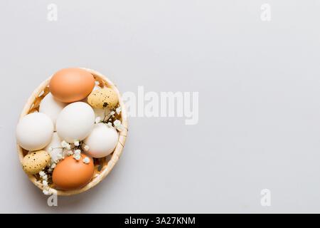 Happy Easter composition. Easter eggs in basket on colored table with gypsophila. Natural dyed colorful eggs background top view with copy space. Stock Photo